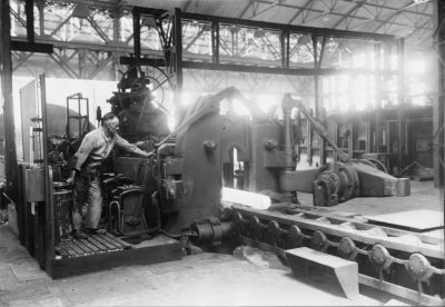 zu sehen ist eine Maschine und ein gluehend heißer Stahlblock im frueheren Bouser Werk