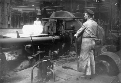 zu sehen ist auf diesem alten Foto die Einfuhr eines dicken gluehenden Stahlblocks zur Weiterverarbeitung
