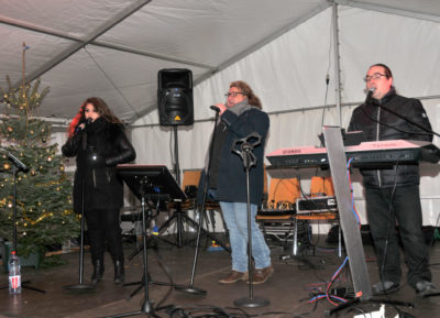 zu sehen sind zwei Musiker und eine Saengerin bei der Live Musik am Bouser Weihnachtsmarkt